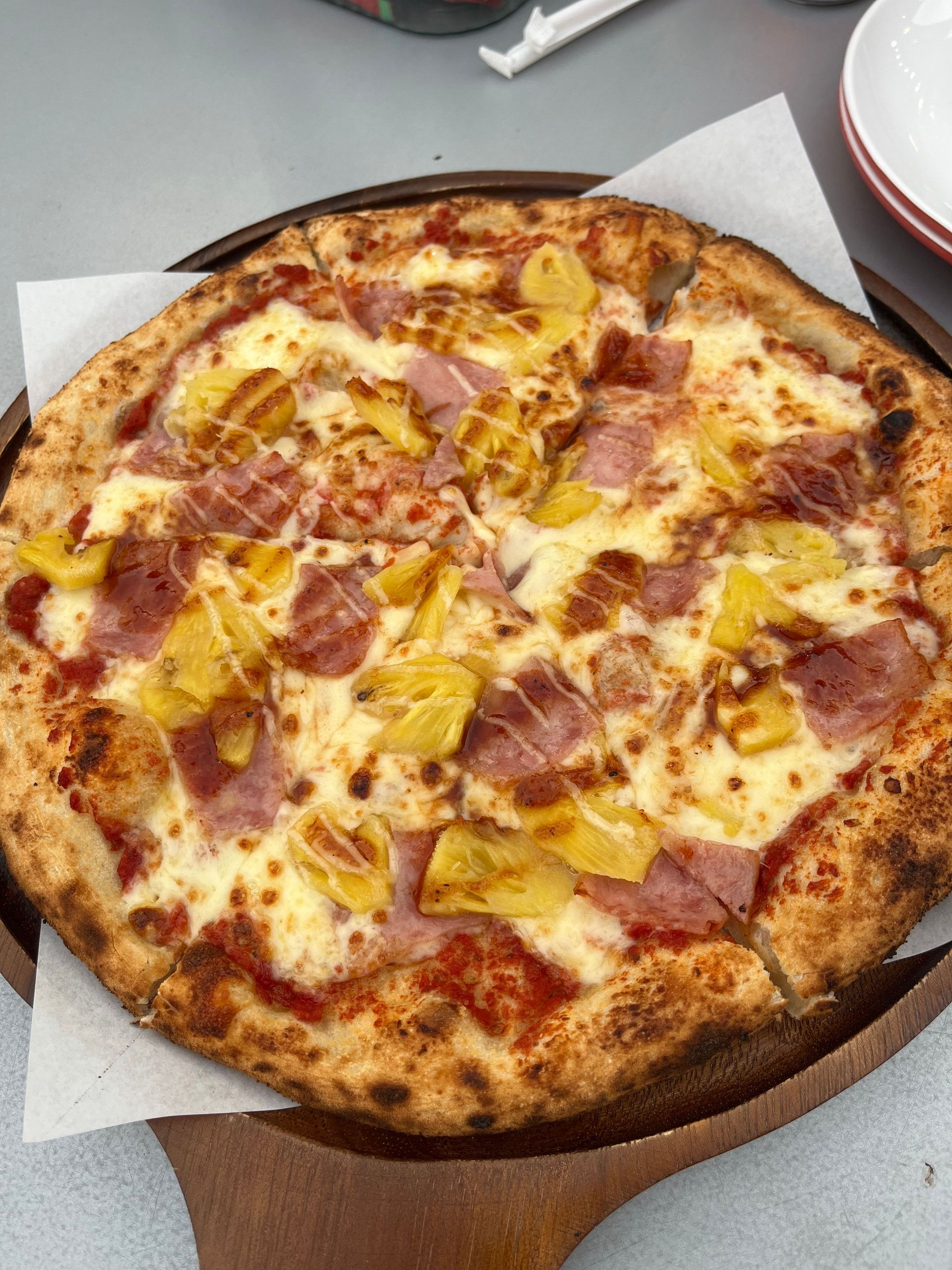 Delicious Hawaiian pizza topped with ham and pineapple on a wooden platter.